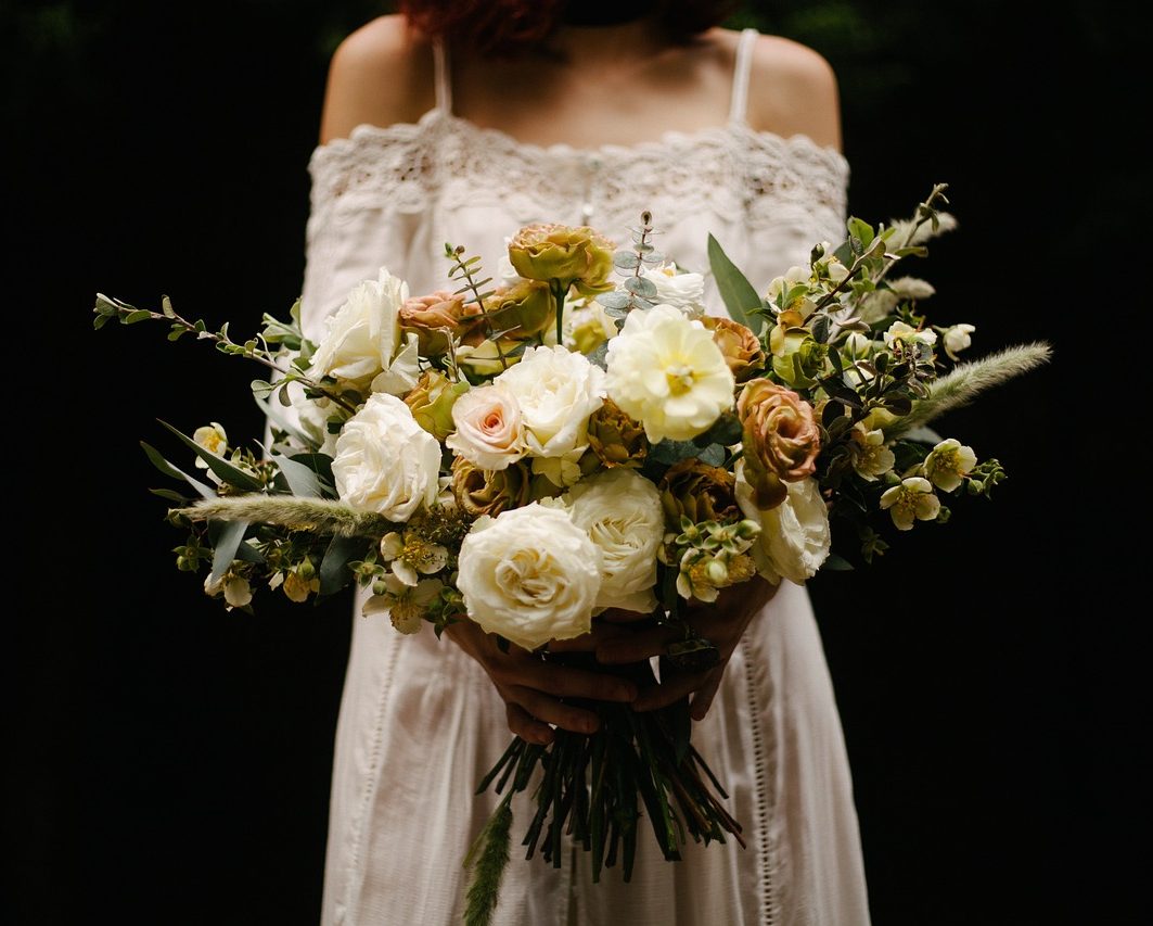 Eine Person hält einen bunten Blumenstrauß mit weißen und pastellfarbenen Blüten.